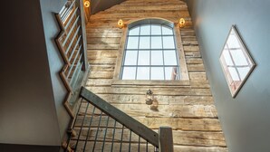 A spiral staircase with wooden steps and metal railings, leading to a loft area with a large window and a lantern. - Rustic Luxury Barn Retreat in Pray, Montana – Family & Pet Friendly (Livingston)