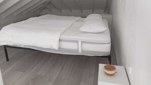 A small, white, single-bed room with a sloped ceiling and a wooden floor. - 1 bedroom apartment in marigot (Marigot)