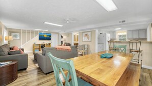 A spacious living room with a wooden dining table, grey sofas, and a TV mounted on the wall.