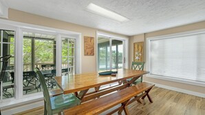 A dining area with a wooden table and benches, large windows, and a view of the outdoors.