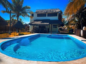 Una piscina con un edificio de techo de paja al fondo.