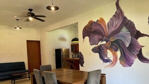 Een eetgedeelte met een houten tafel en stoelen, een plafondventilator en een grote muurschildering van een vis.
