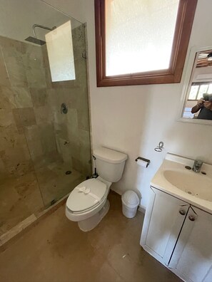 Un baño con cabina de ducha de vidrio, inodoro, lavamanos y espejo.