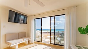 Ein modernes Wohnzimmer mit Fernseher, einer Couch und einer großen Schiebeglastür, die auf einen Balkon mit Meerblick führt.