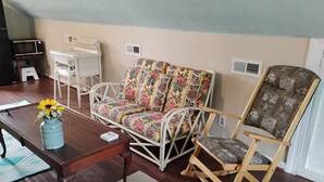 A room with a wooden coffee table, a rocking chair, a sofa with floral upholstery, and a wicker chair.
