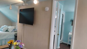 A bedroom with a bed, a TV mounted on the wall, a vase with flowers on the nightstand, and a door leading to another room.