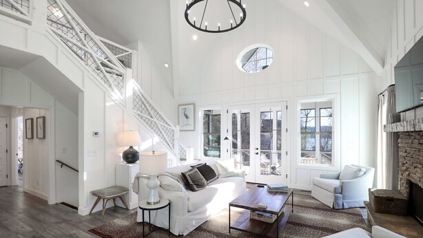 A spacious living room with a high ceiling, a staircase, and a fireplace.