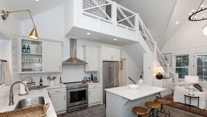 A modern kitchen with white cabinetry, a stainless steel range, and a central island with stools.