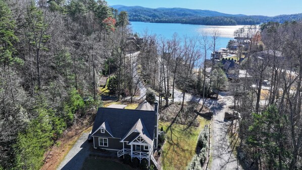 A house with a gabled roof, surrounded by a forested area and a body of water in the background. - Scenic 4BR 2BA Lake Burton Home (Tiger)