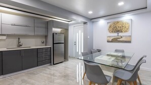 A modern kitchen with grey cabinets, a stainless steel refrigerator, and a glass dining table with grey chairs. - Sabana River Villa Las Paylas (Bo Sabana Sec The Widows)