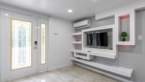 A modern living room with a built-in TV, white shelving, and an air conditioning unit. - Sabana River Villa Las Paylas (Bo Sabana Sec The Widows)