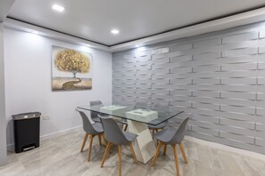 Una sala de reuniones moderna con una mesa de vidrio, sillas grises, una pared con diseño de ladrillo y una pintura de un árbol.