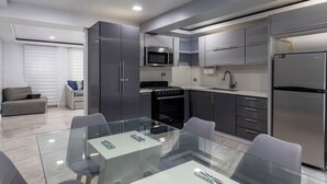 A modern kitchen with stainless steel appliances, grey cabinetry, and a glass dining table. - Sabana River Villa Las Paylas (Bo Sabana Sec The Widows)