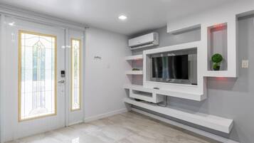 A modern interior with a flat-screen TV mounted on a white wall, a built-in air conditioning unit, and a door with a glass panel.