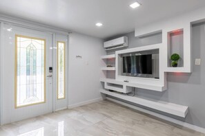 Un interior modern amb un televisor de pantalla plana fixat a una paret blanca, un sistema de climatització integrat i una porta amb un panell de vidre.