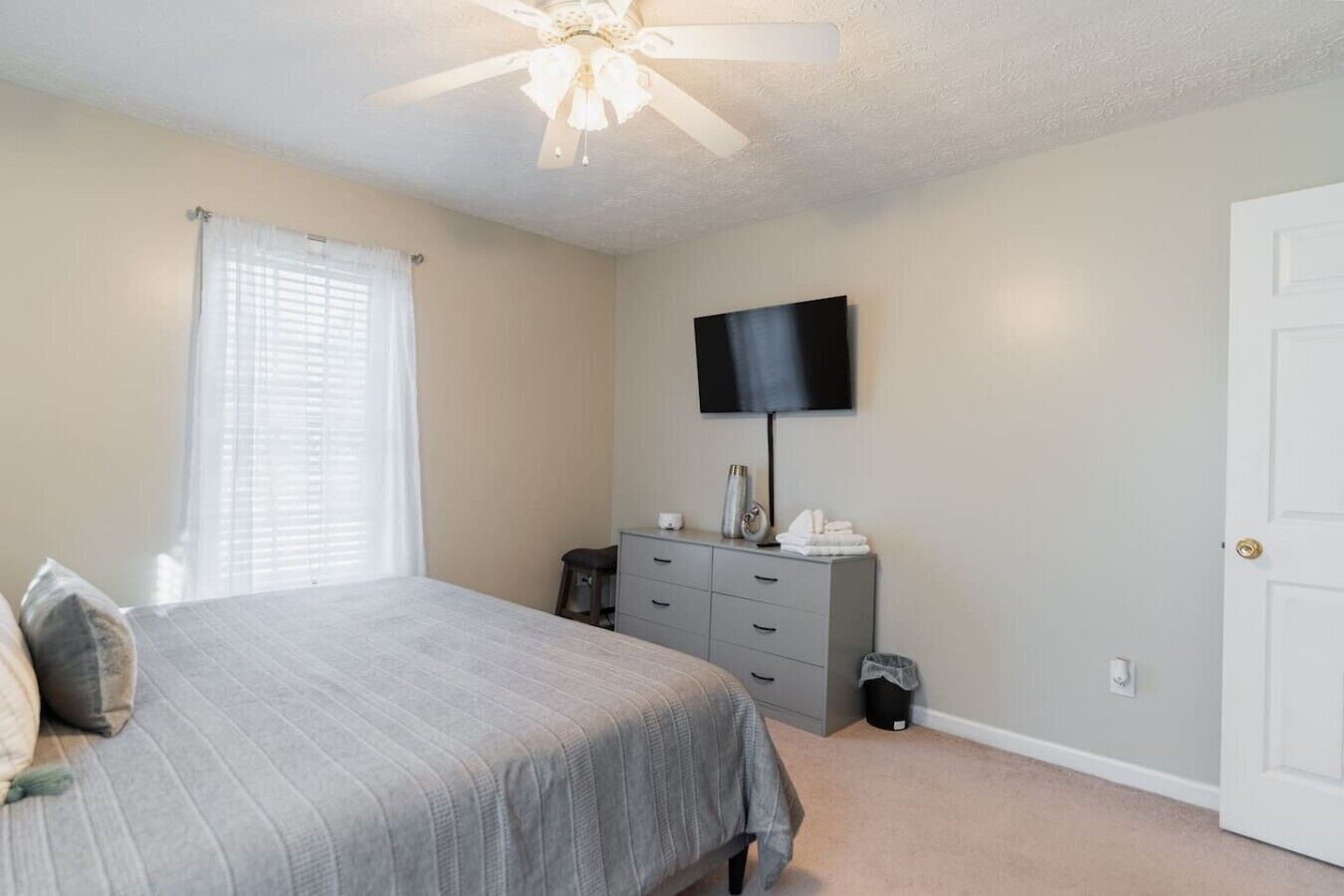 A bedroom with a bed, a dresser, a television, and a ceiling fan.