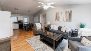 A spacious living room with a dark sofa set, a coffee table, and a fireplace. There is a kitchen in the background with white cabinets and a dining area. - Spacious 3bd/2ba near Casino (Danville)