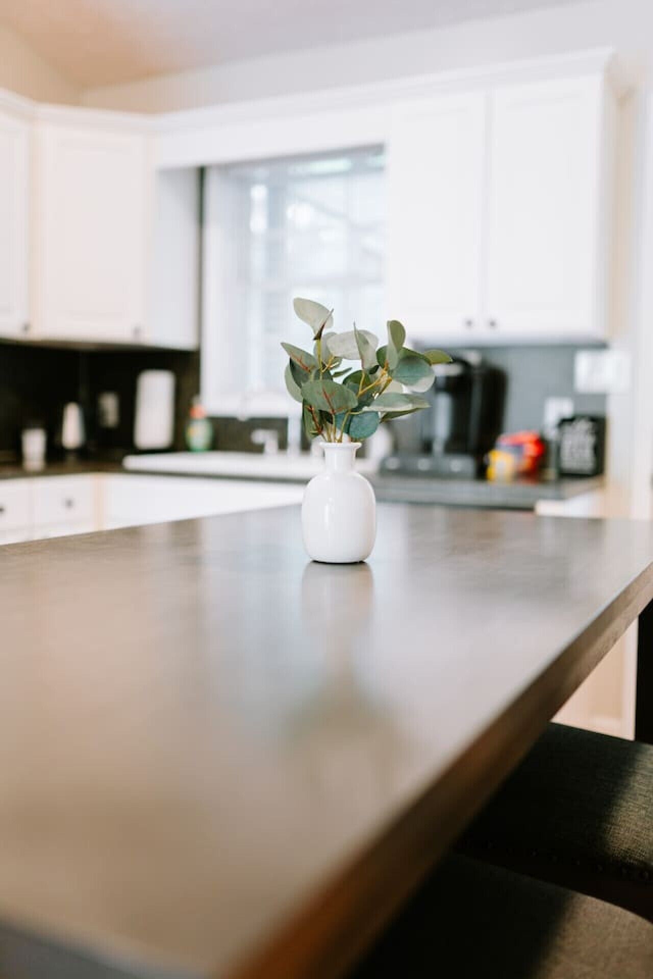 A kitchen with white cabinets, a wooden countertop, and a white vase with green leaves.