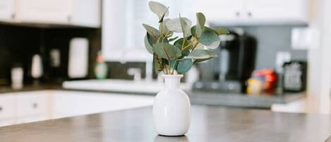 A kitchen with white cabinets, a wooden countertop, and a white vase with green leaves.