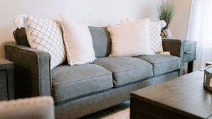 A grey sofa with patterned cushions, a wooden side table, and a small plant in a corner. - Spacious 3bd/2ba near Casino (Danville)