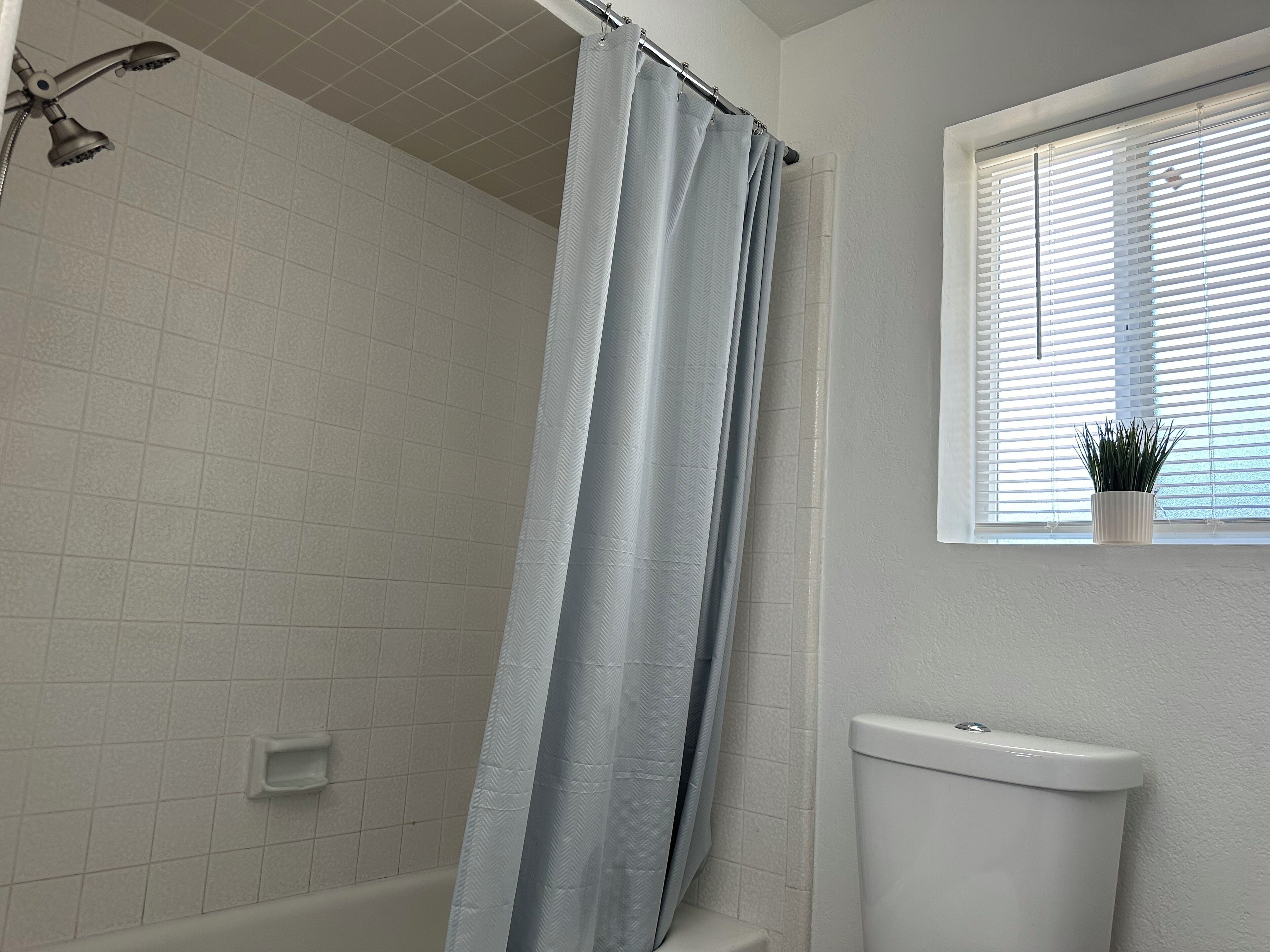 Een badkamer met een douche, toilet en een raam met zonwering.