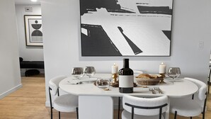 Ruokailutila, jossa on pyöreä pöytä, valkoiset tuolit, viinipullo, kynttilöitä ja leipäkori.