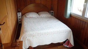 A wooden-paneled room with a bed, a small bedside table, and a window with curtains.
