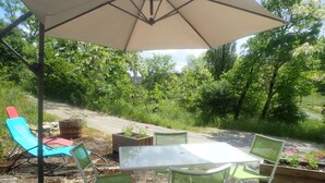 An outdoor patio area with a table and chairs, surrounded by greenery and a dirt path.