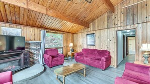 Ein gemütliches Blockhaus-Interieur mit Holzwänden, Kamin, Fernseher und bequemen Sitzmöglichkeiten.