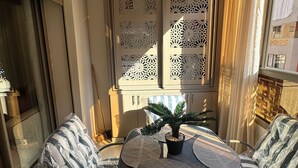 A balcony with a round table, two chairs, a potted plant, and decorative window screens. - Luxury Apartment in Central Marrakech - Pool & Fast Wi-Fi (Marrakesh)