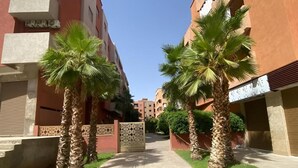 A pathway flanked by palm trees and buildings with a gate in the center. - Luxury Apartment in Central Marrakech - Pool & Fast Wi-Fi (Marrakesh)