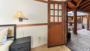 Een kamer met een houten deur, een bed met hoofdeinde, een nachtkastje en een lamp.