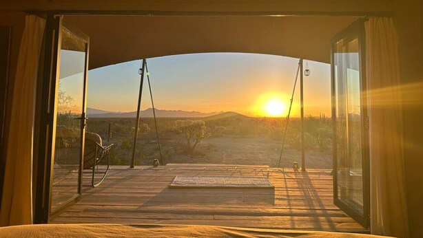 A room with a large window, a bed, and a view of a sunset over a desert landscape. - Tent Cholla, occupancy near Saguaro NP (Marana)