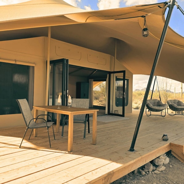 Un patio al aire libre con una mesa y sillas de madera, una lámpara colgante y vistas al paisaje desértico.