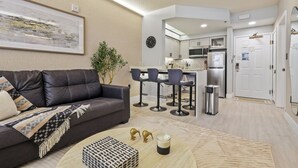 Una sala de estar moderna con un sofá, una mesa de centro y una zona de cocina con taburetes de bar.
