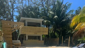 A pool area with a lounge chair, a wooden deck, and a modern building in the background. - Garden of Eden Hotel (Vega Alta)