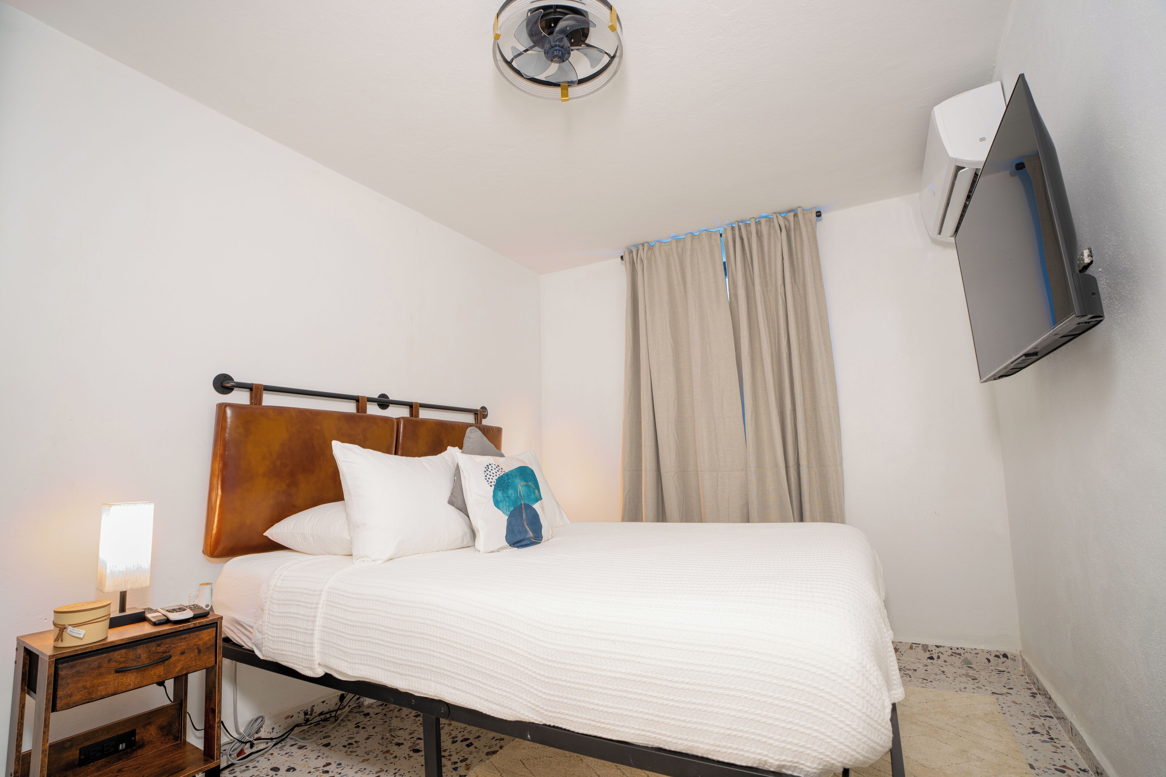 A neatly made bed with white bedding, a wooden headboard, and a bedside table with a lamp and a phone.