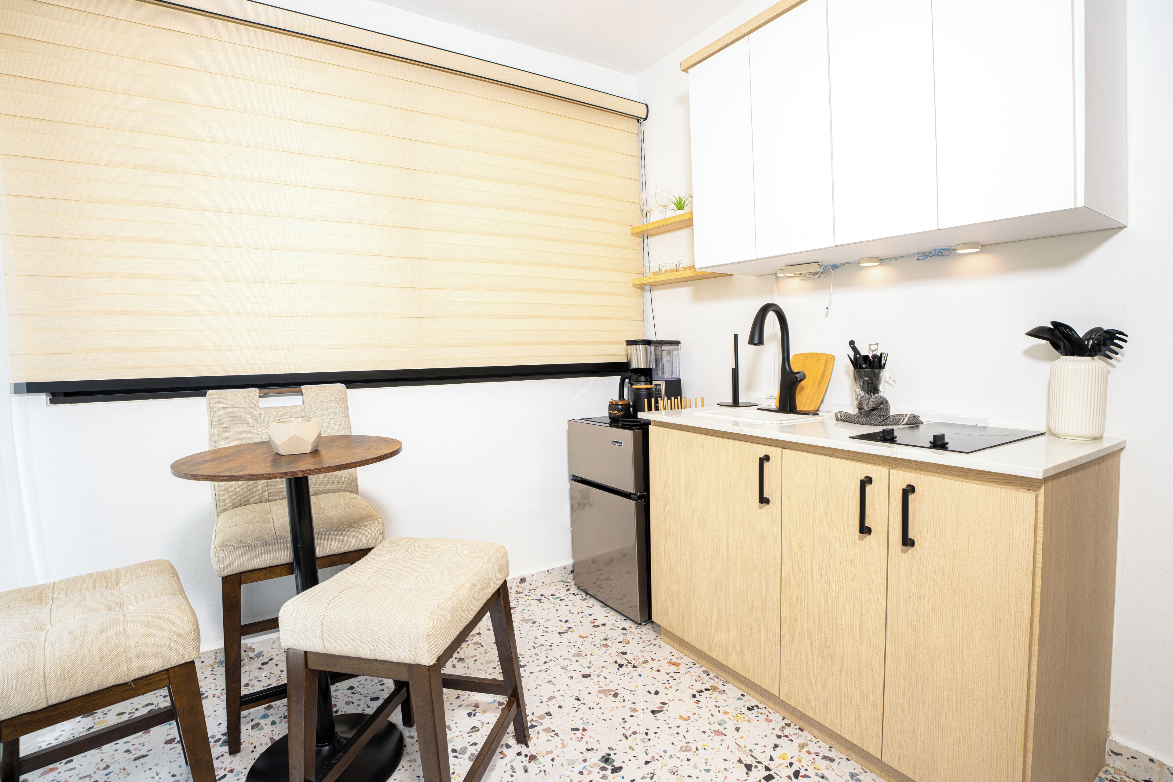 Uma cozinha compacta com uma mesa redonda, duas cadeiras, fogão embutido e bancada com pia e diversos utensílios.