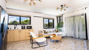A modern kitchen with a refrigerator, microwave, and sink. There is a sofa with cushions, a coffee table, and a plant. - Garden of Eden Hotel (Vega Alta)