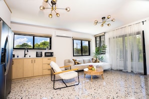 Un espacio habitable moderno con cocina, sofá y comedor, que cuenta con ventanas amplias, una lámpara de techo y un suelo moteado.