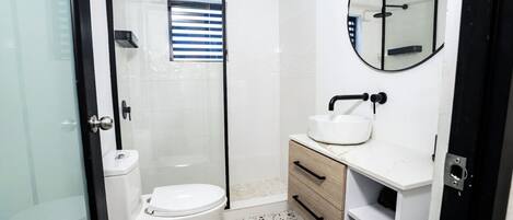 A modern bathroom with a glass-enclosed shower, a white toilet, a sink with a mirror, and a tiled floor.