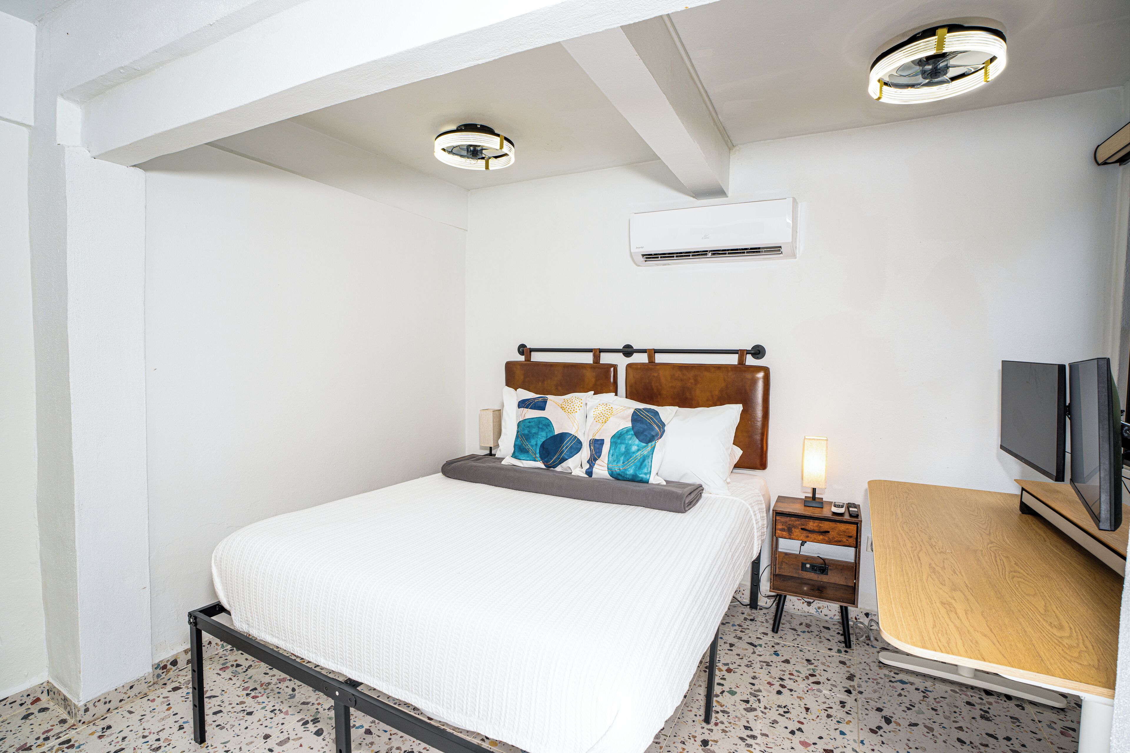 A bedroom with a bed, bedside table, TV, and an air conditioning unit.