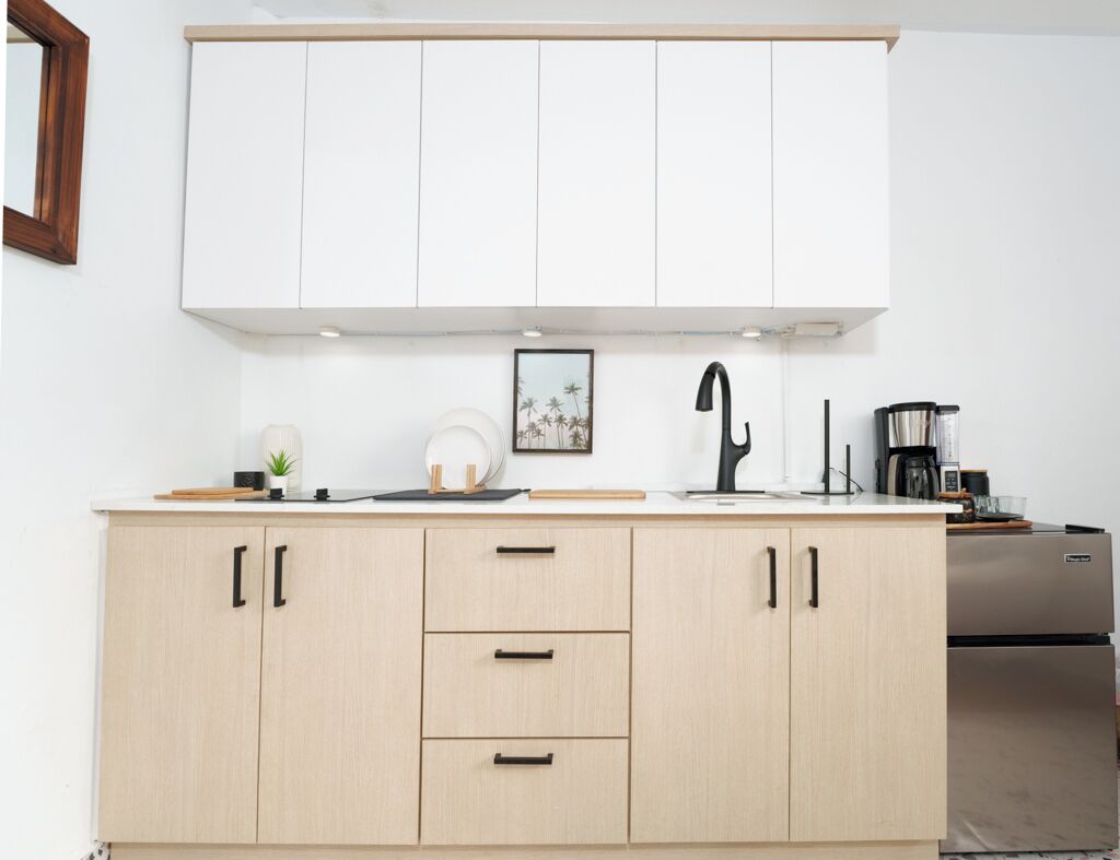 A modern kitchen with light wood cabinets, a black faucet, and a stainless steel refrigerator.