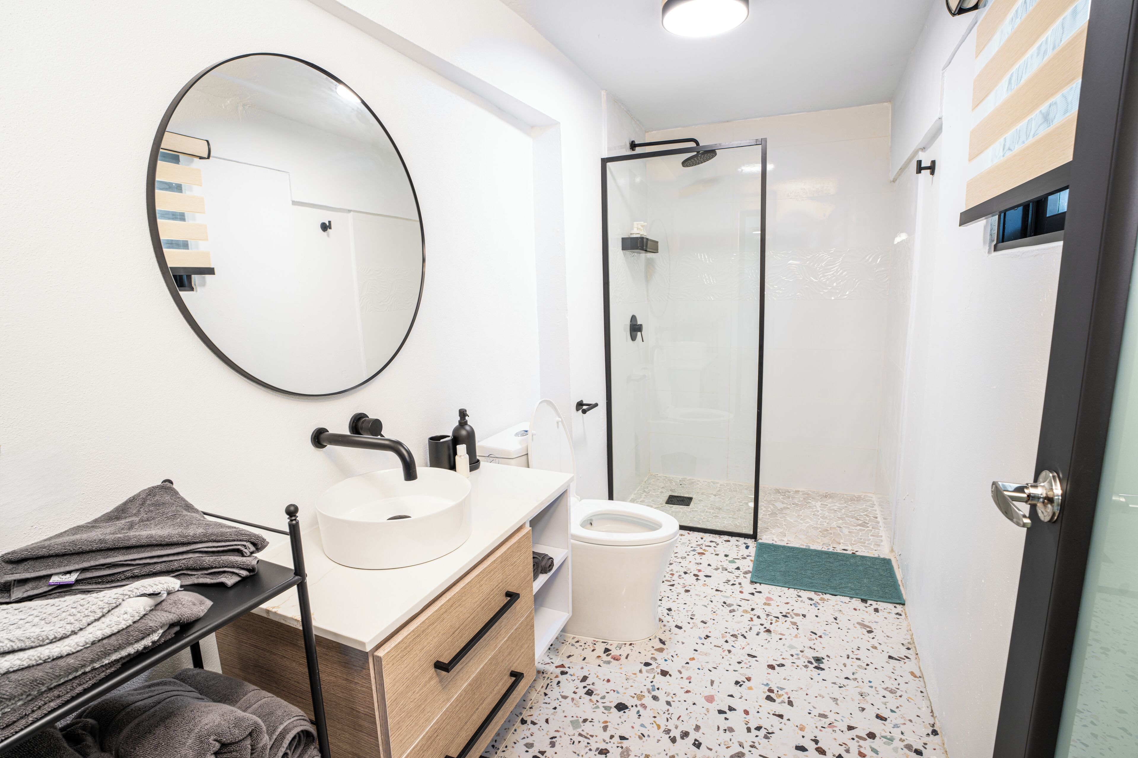 A modern bathroom with a round mirror, a sink, a toilet, and a shower area.