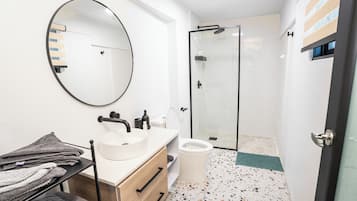 A modern bathroom with a round mirror, a sink, a toilet, and a shower area.