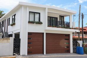 A modern two-story house with a white facade, large wooden garage doors, and a balcony with potted plants. - Garden of Eden Hotel (Vega Alta)
