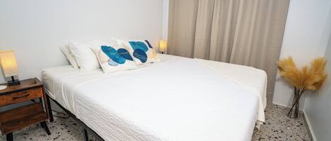 A bedroom with a bed, a nightstand, a lamp, and a vase with dried plants.