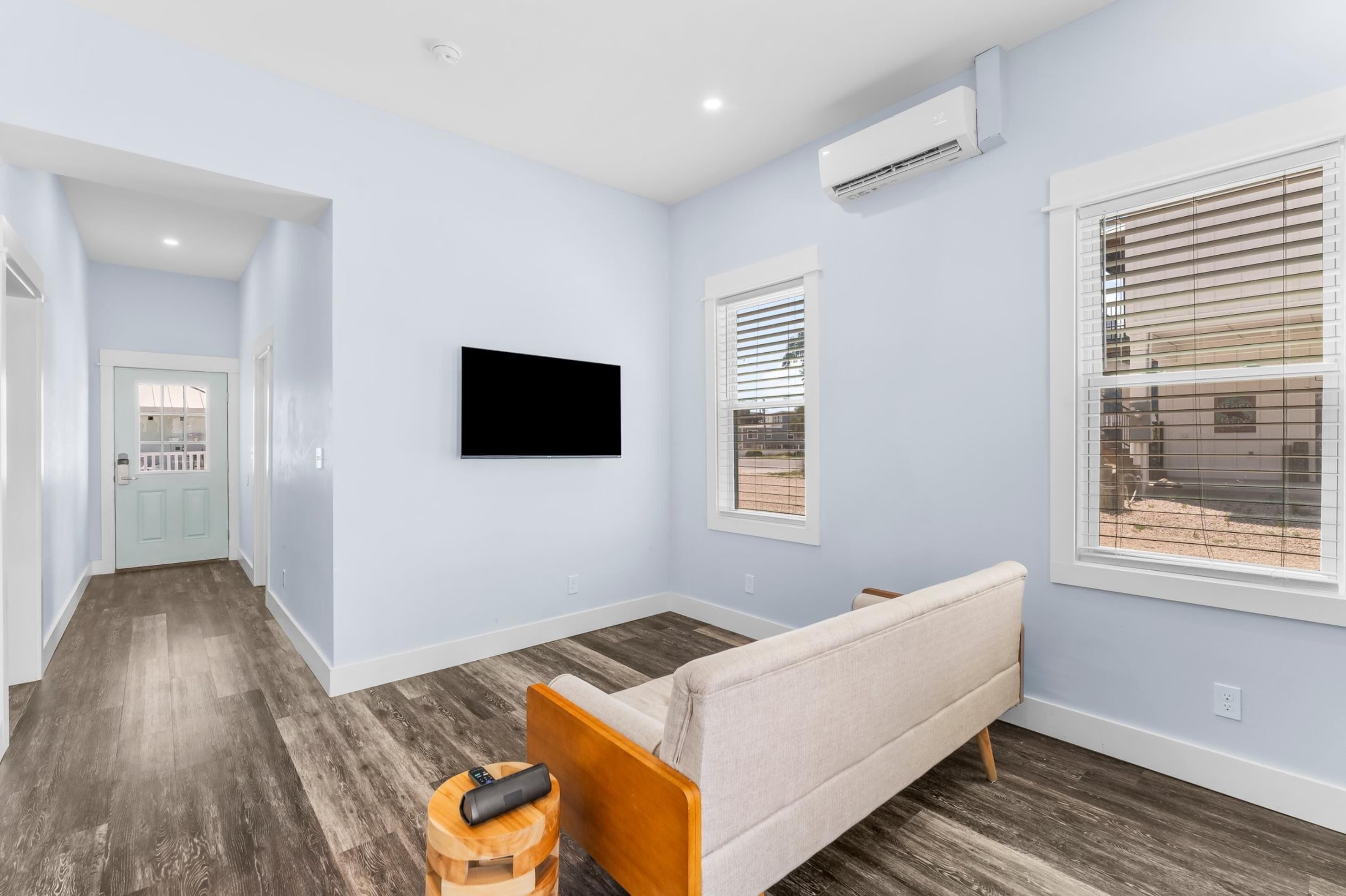 Een moderne woonkamer met een bank, een aan de muur bevestigde televisie en een raam met zonwering.