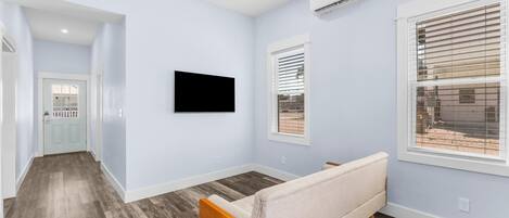 Een moderne woonkamer met een bank, een aan de muur bevestigde televisie en een raam met zonwering.