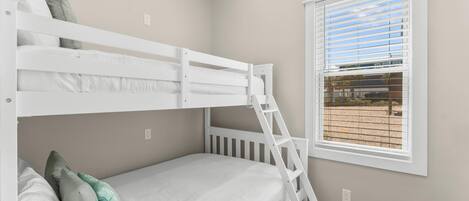 Quarto com beliche, escada, janela com persianas e vista para área externa.